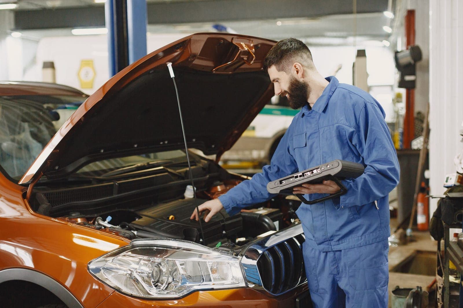 Mécanicien en combinaison bleue, valise de diagnostic à la main, penché sur un moteur